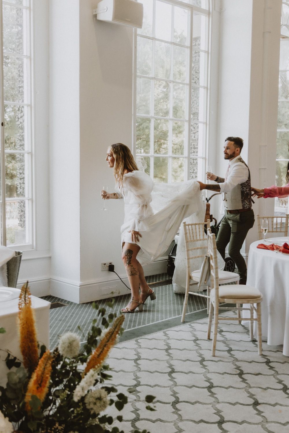 Wedding reception candid moments with guests in an elegant white room with floral decorations.