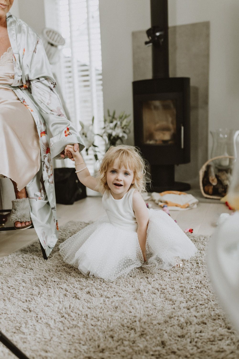 Young flower girl in white dress playing on plush carpet during wedding preparations.