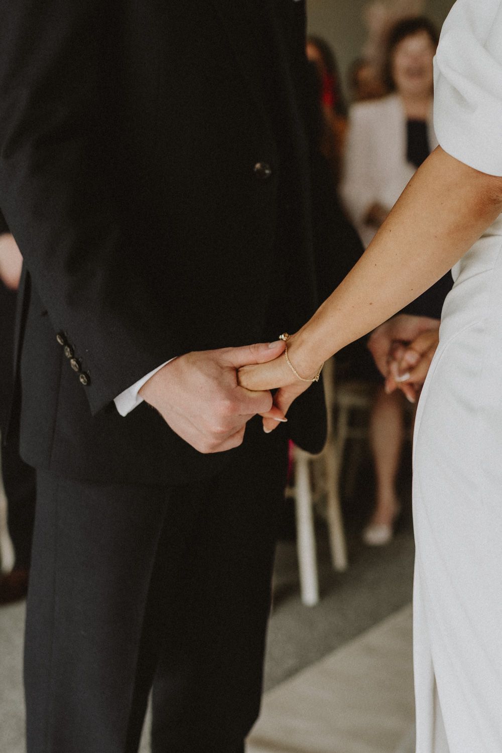 Close-up of couple holding hands during wedding ceremony with guests in background.