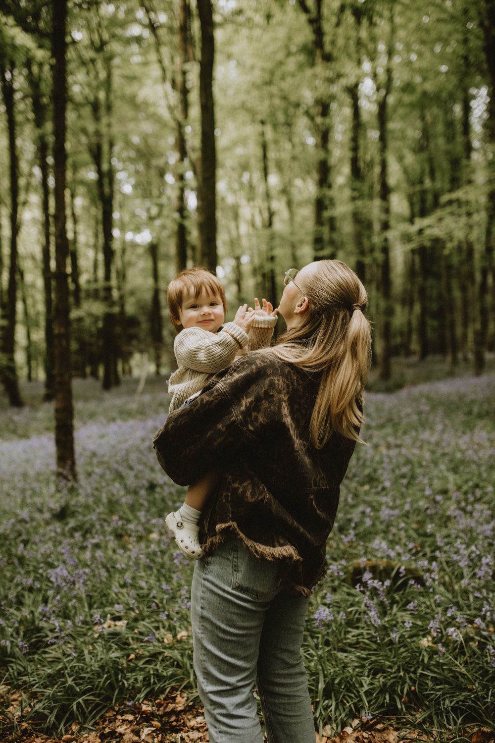 Parent and child sharing playful moments in a forest surrounded by spring bluebells.