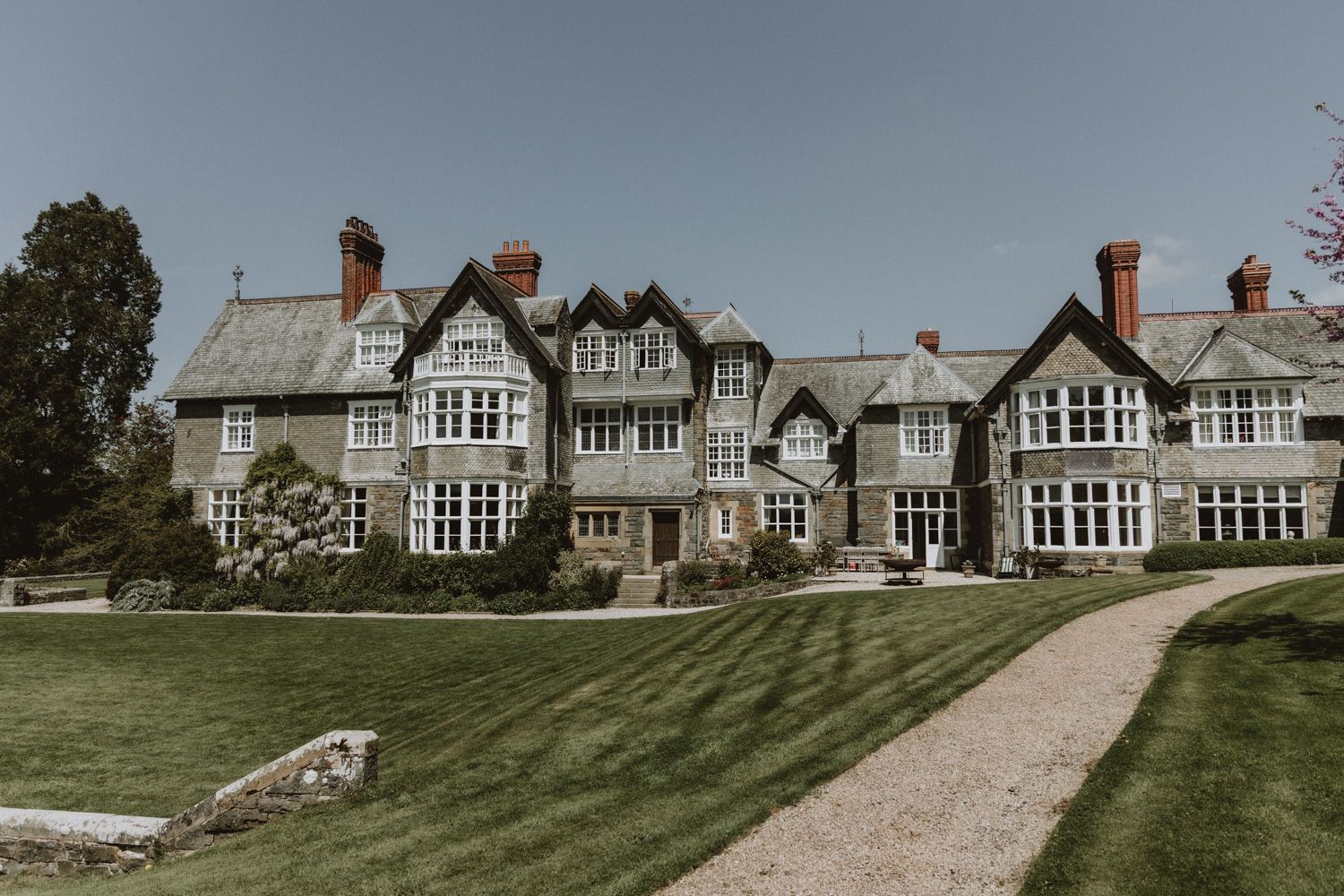Elegant Tudor-style manor house with manicured lawn and gravel pathway.