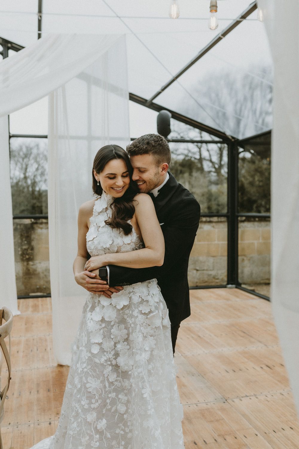 An intimate moment captured in a sunlit wedding venue with flowing white curtains and rustic decor.