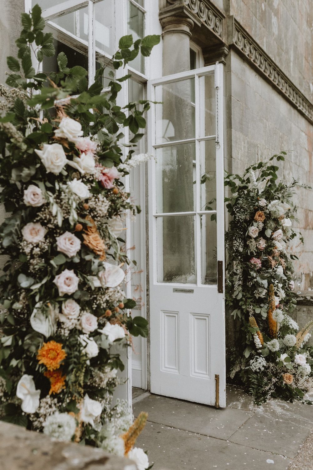 White and orange floral arch arrangement framing an elegant doorway entrance.