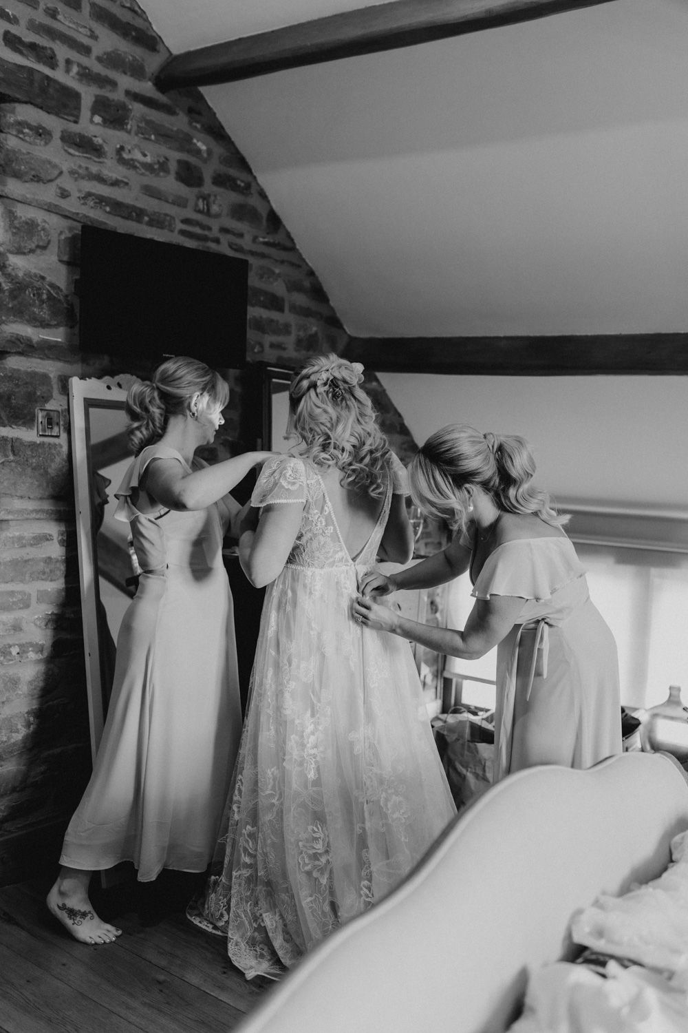 Wedding preparation scene in a rustic brick room with white gowns.