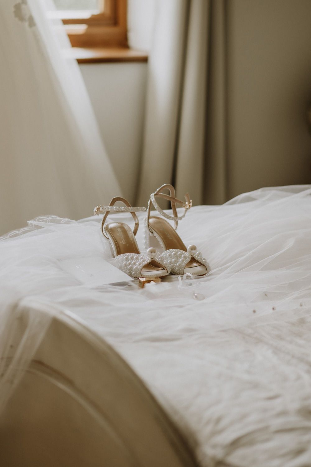 Delicate white lace wedding shoes resting on soft white bedding.