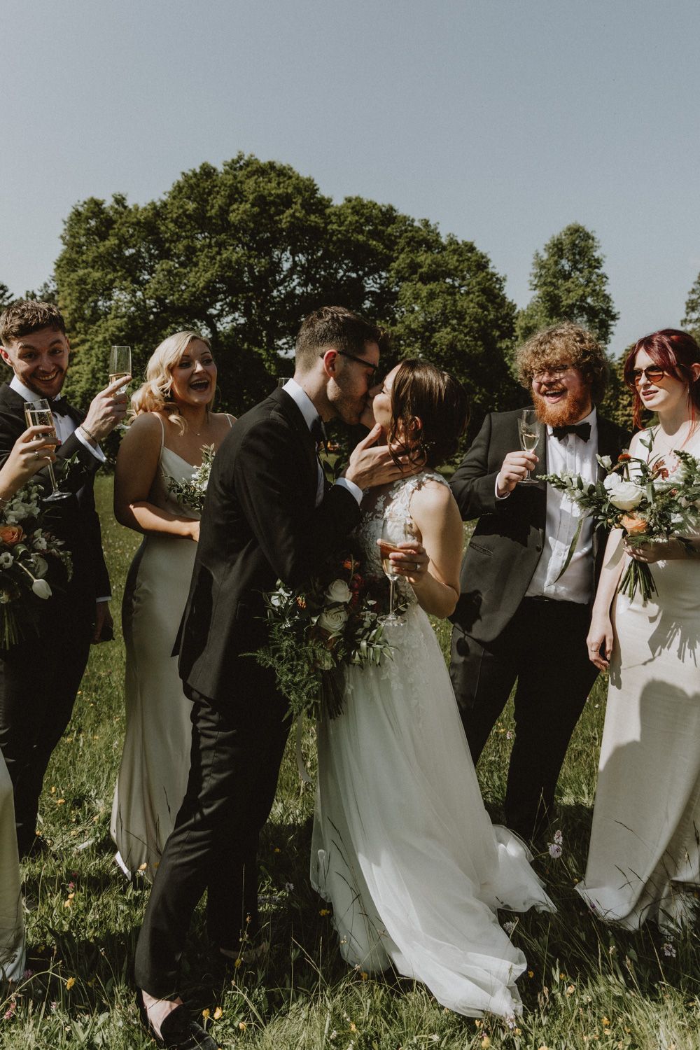 Wedding party celebrating outdoors with champagne glasses and bouquets.