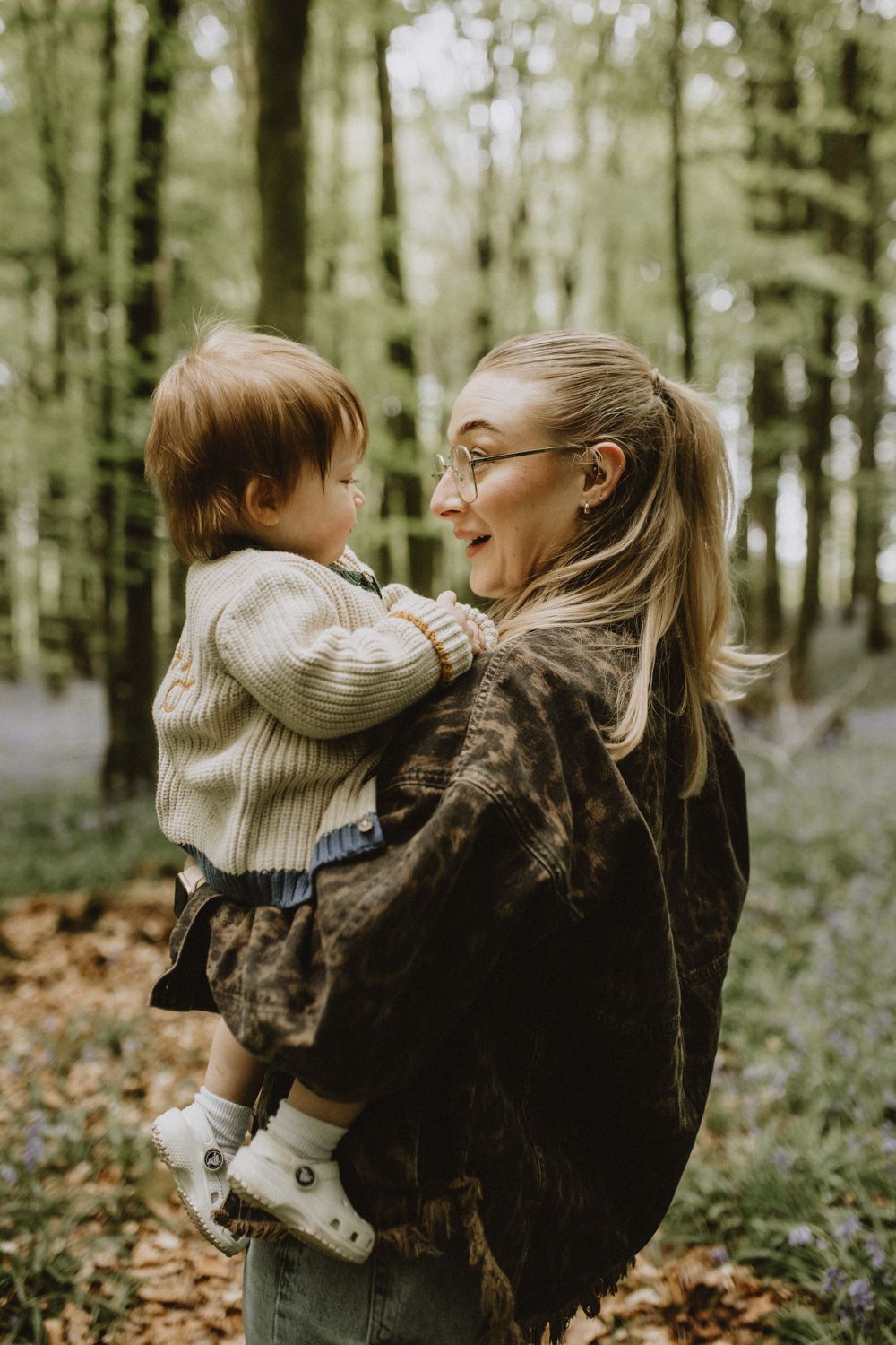 Parent and small child share joyful moments together in a serene woodland setting with bluebells and fallen leaves.