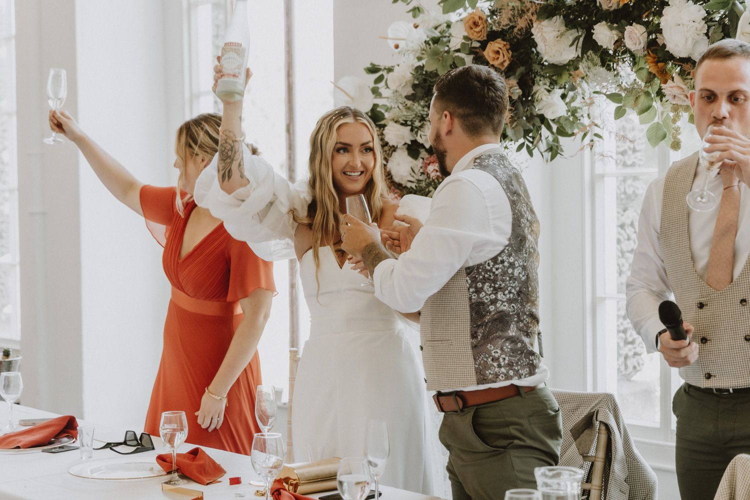 Wedding celebration with guests in a bright venue decorated with white floral arrangements.