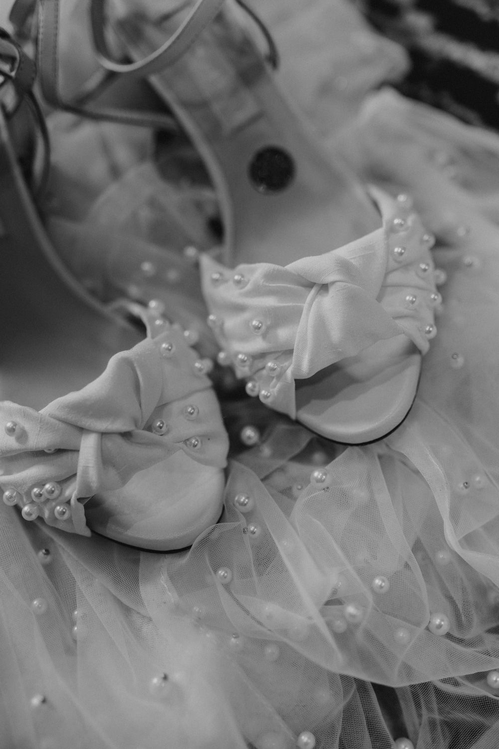 Elegant bridal shoes with pearl details rest on delicate tulle fabric in black and white.