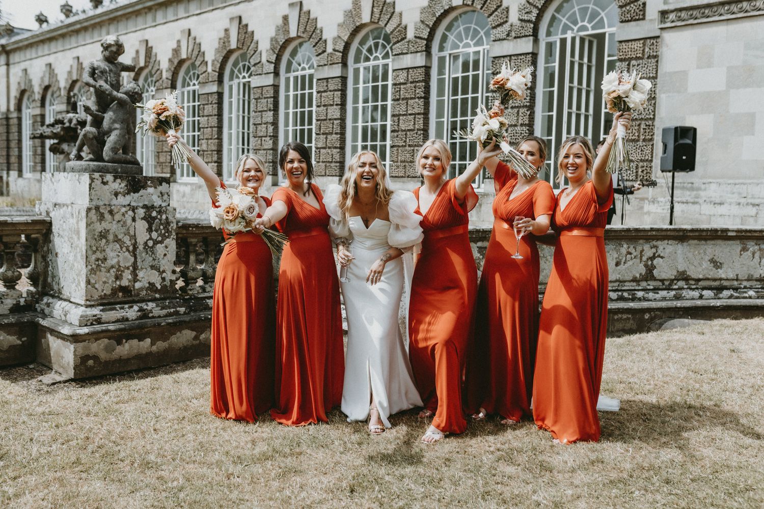Wedding party posing in front of historic building with bridesmaids in matching orange dresses.