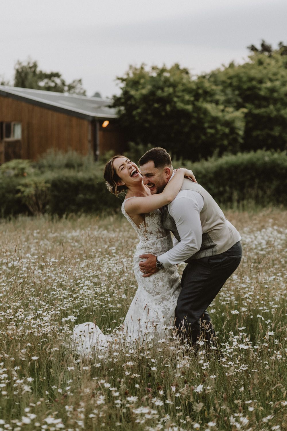 Romantic wedding moment captured in a wildflower meadow with rustic barn in background.