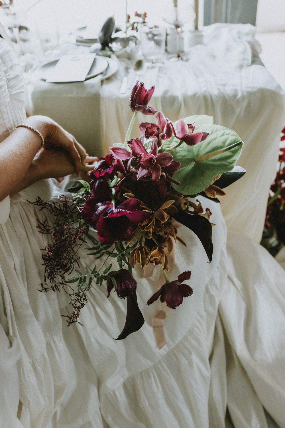 A hand holds a beautiful bouquet of deep red flowers against flowing white fabric.