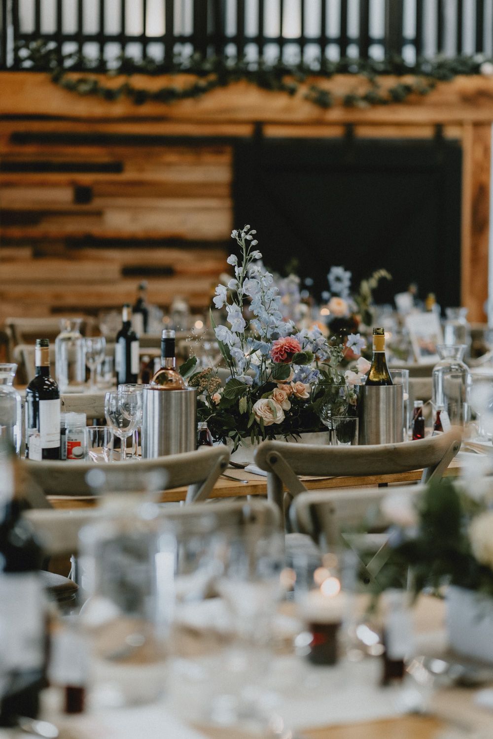 Elegant wedding reception table setting with delicate floral centerpiece and rustic wooden backdrop.