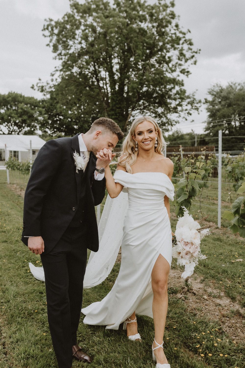 Newlyweds pose playfully in vineyard setting.