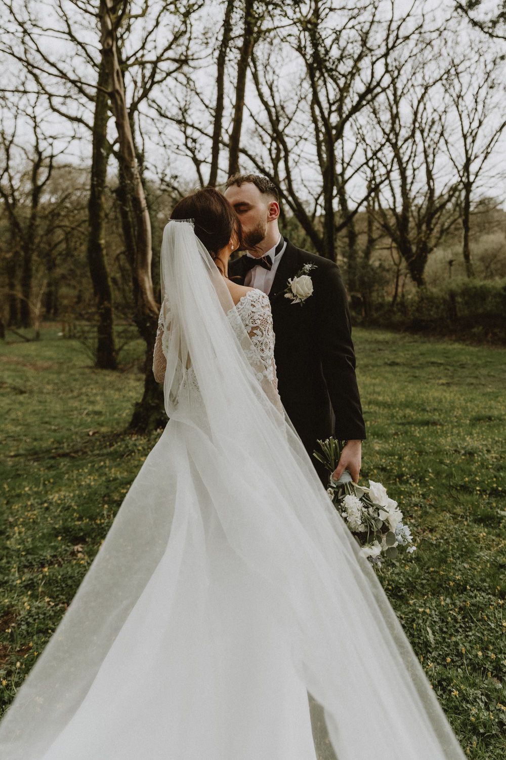 A flowing white wedding dress and veil create ethereal movement in a forest setting.