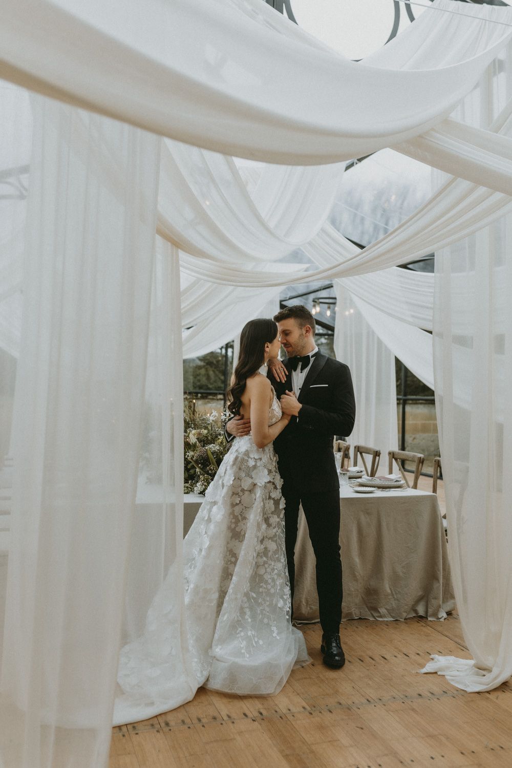 Wedding reception space decorated with flowing white fabric drapes and soft lighting.