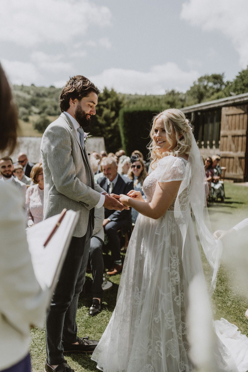 A wedding ceremony takes place outdoors with guests watching the couple exchange vows.