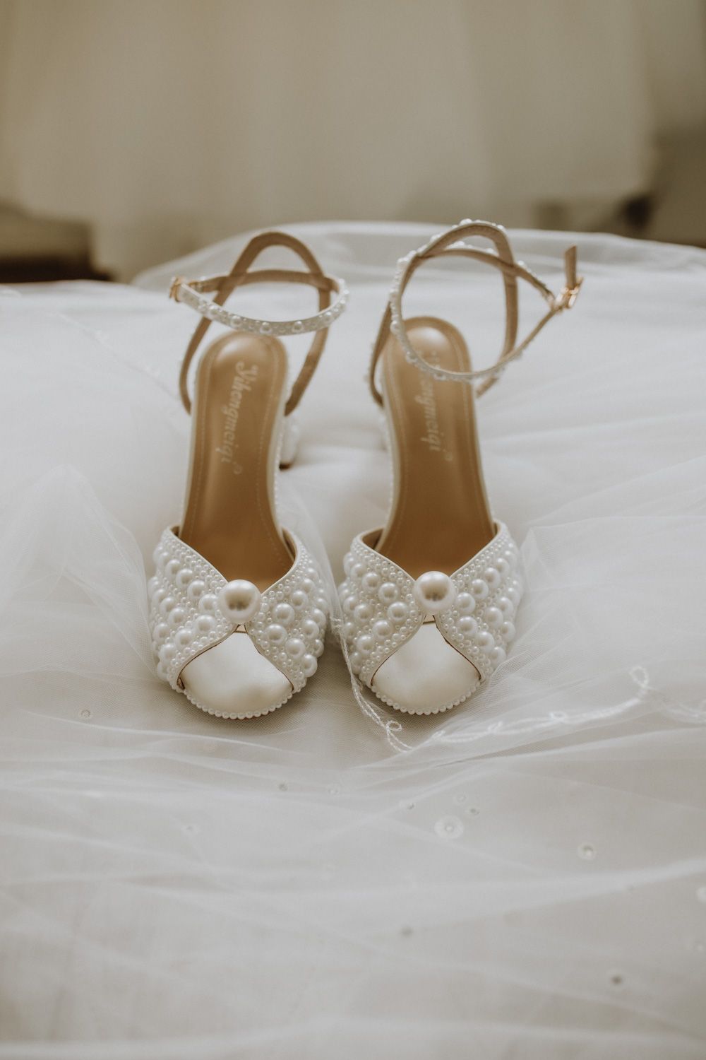 Elegant white bridal shoes with pearl embellishments displayed on white fabric.