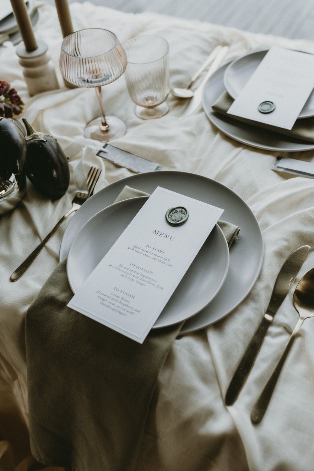 Minimalist wedding table setting with white plates, menu cards, and wax seals.