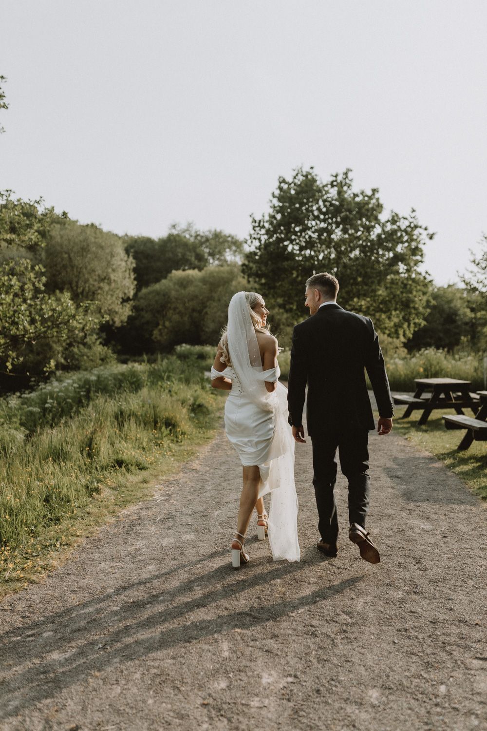 Newlyweds walking down a scenic path surrounded by lush greenery during golden hour.