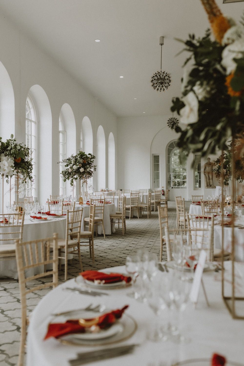 Sophisticated wedding reception hall with arched windows, floral centerpieces and elegant place settings.