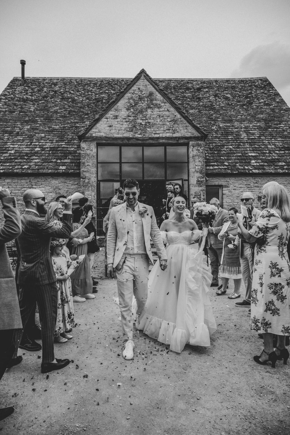 Black and white photo of wedding guests gathered outside a rustic stone barn venue.