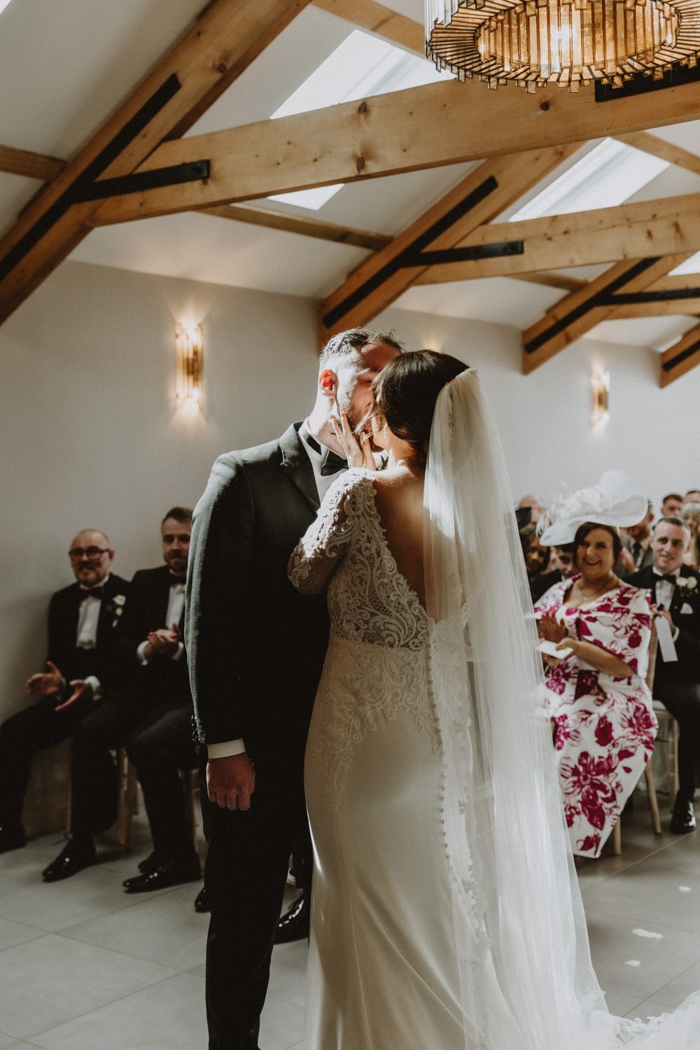 Intimate wedding ceremony moment under wooden beam ceiling with elegant chandelier.