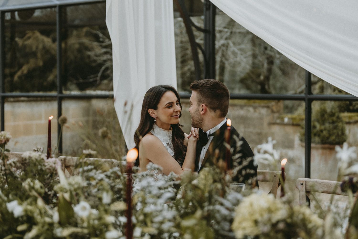 Romantic wedding couple shares intimate moment under floral-decorated tent.