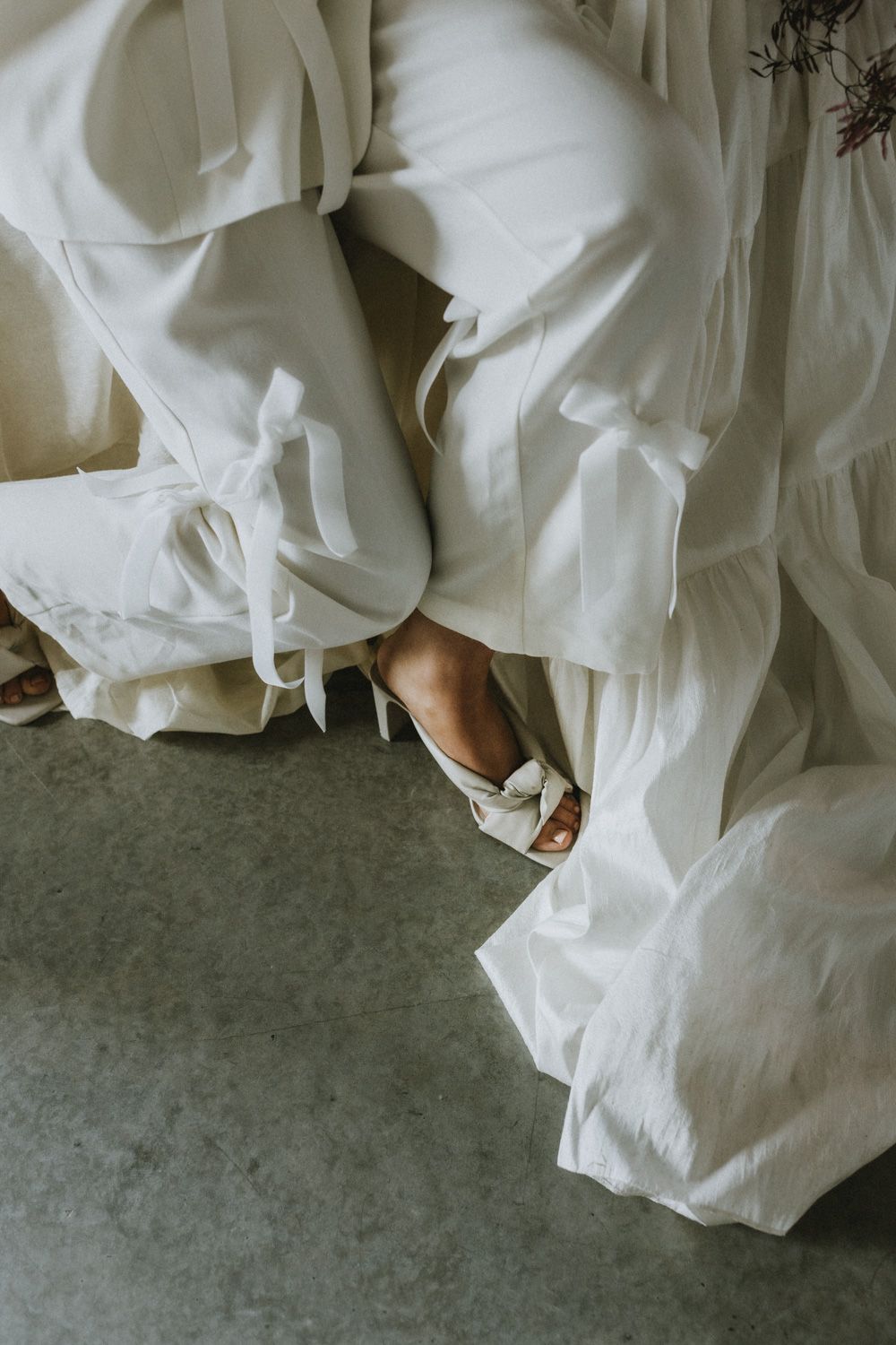 White wedding dress fabric flows over white shoes on a concrete floor.