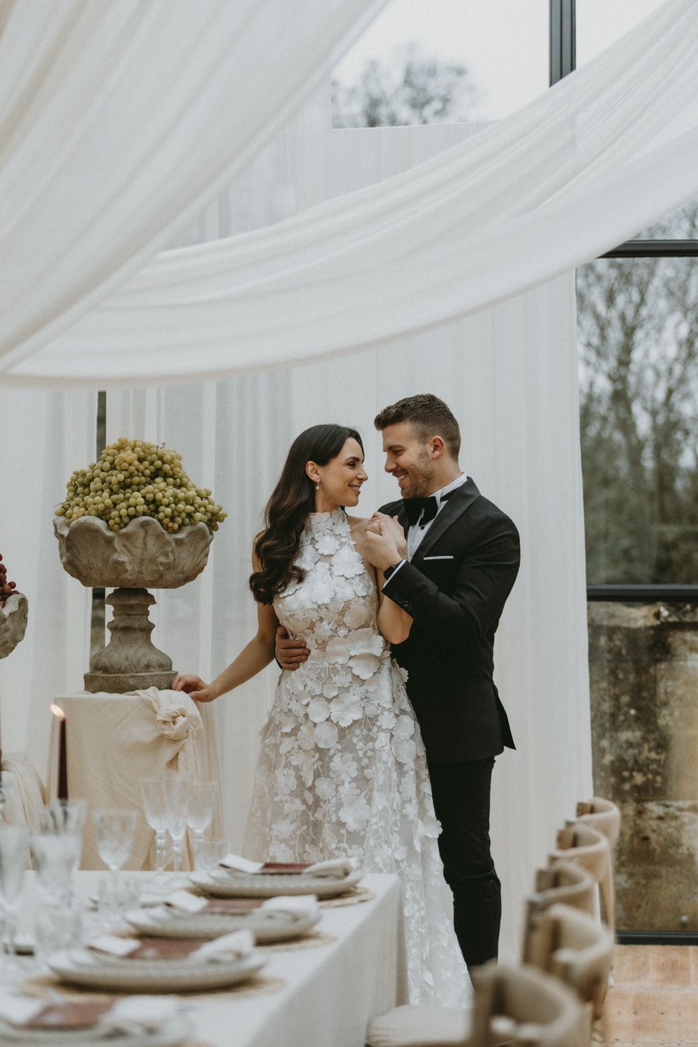 A romantic wedding reception setup with elegant draping and a beautifully set table in an airy venue.