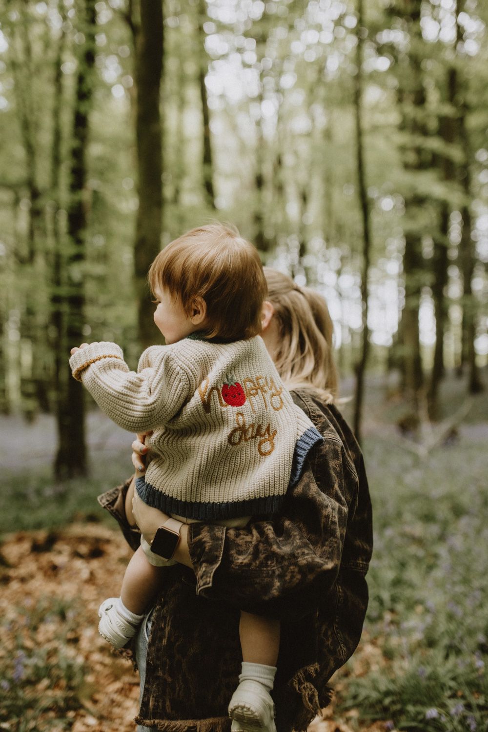 A playful moment captured in a forest filled with bluebells, showing joyful interaction between parent and child.