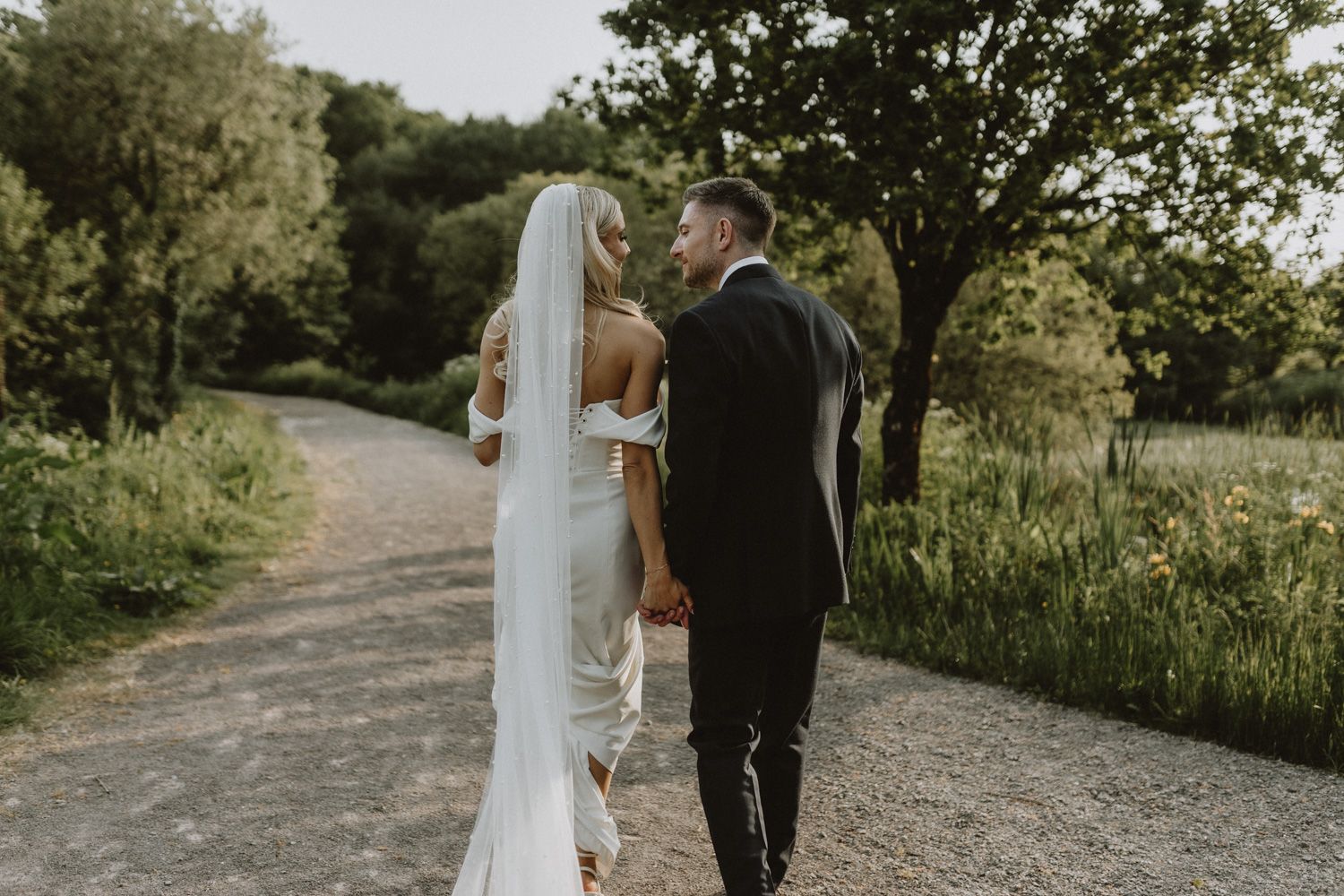 Couple in wedding attire walking along a winding path through a natural setting.
