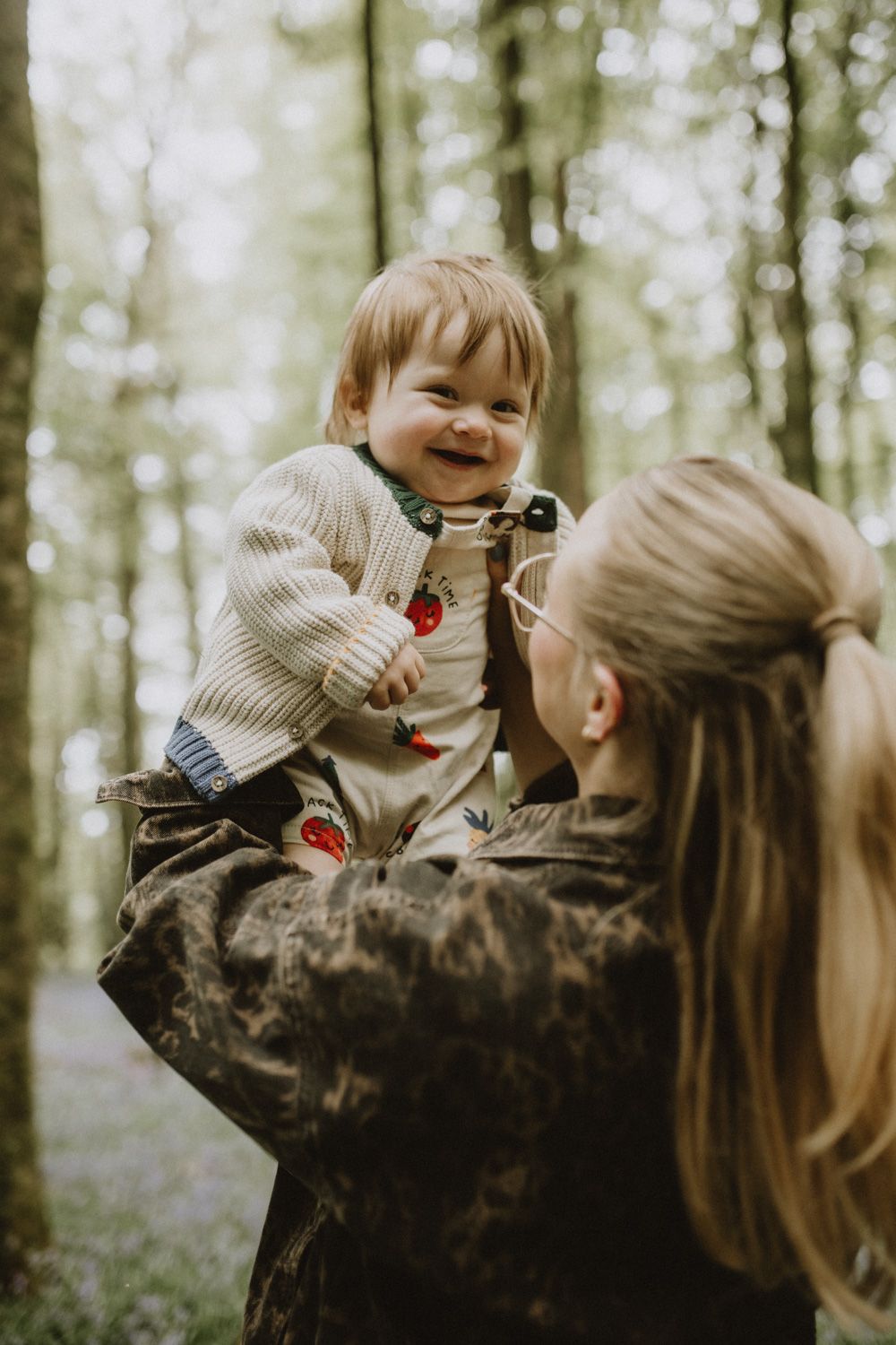 Joyful moment between parent and baby in sunlit forest setting.