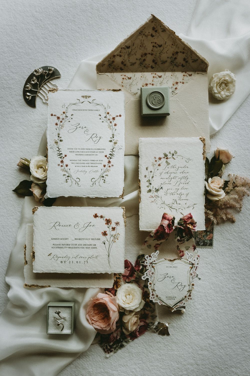 Elegant wedding invitation suite with floral designs and wax seal on white fabric.