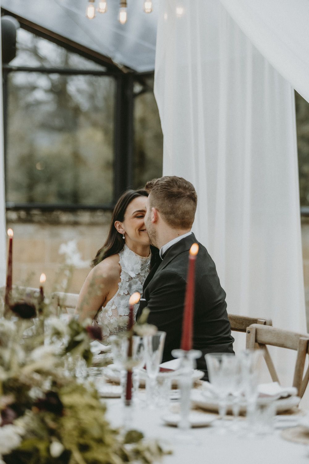 Elegantly draped white fabric frames an intimate wedding reception table setting with glowing candles and floral arrangements.