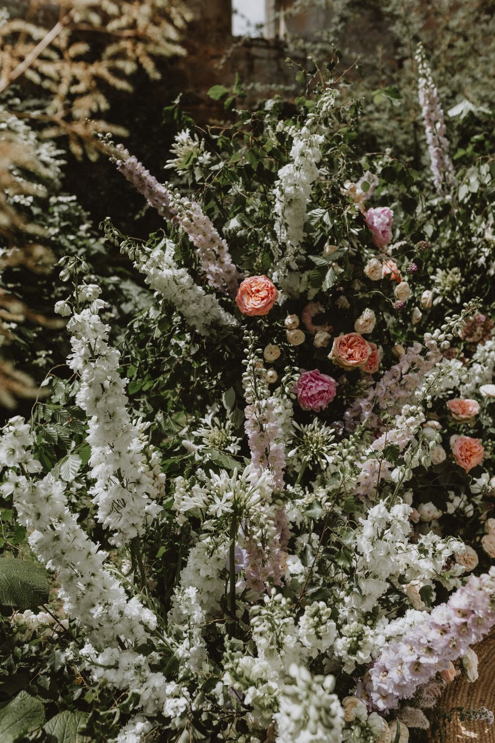 Lush garden arrangement featuring white delphinium spires and peachy roses.