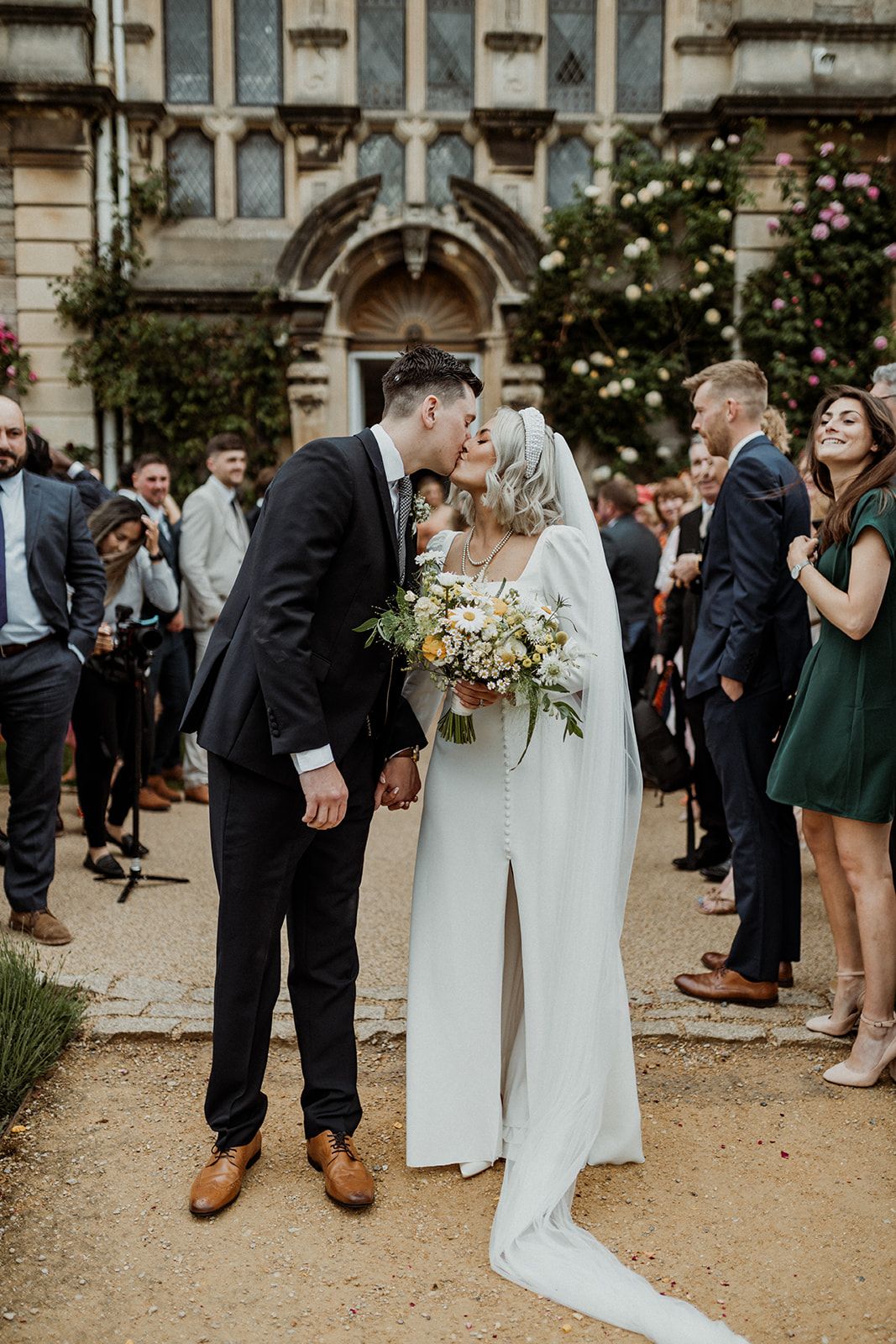 Newlyweds sharing their first kiss outside a historic venue surrounded by guests.
