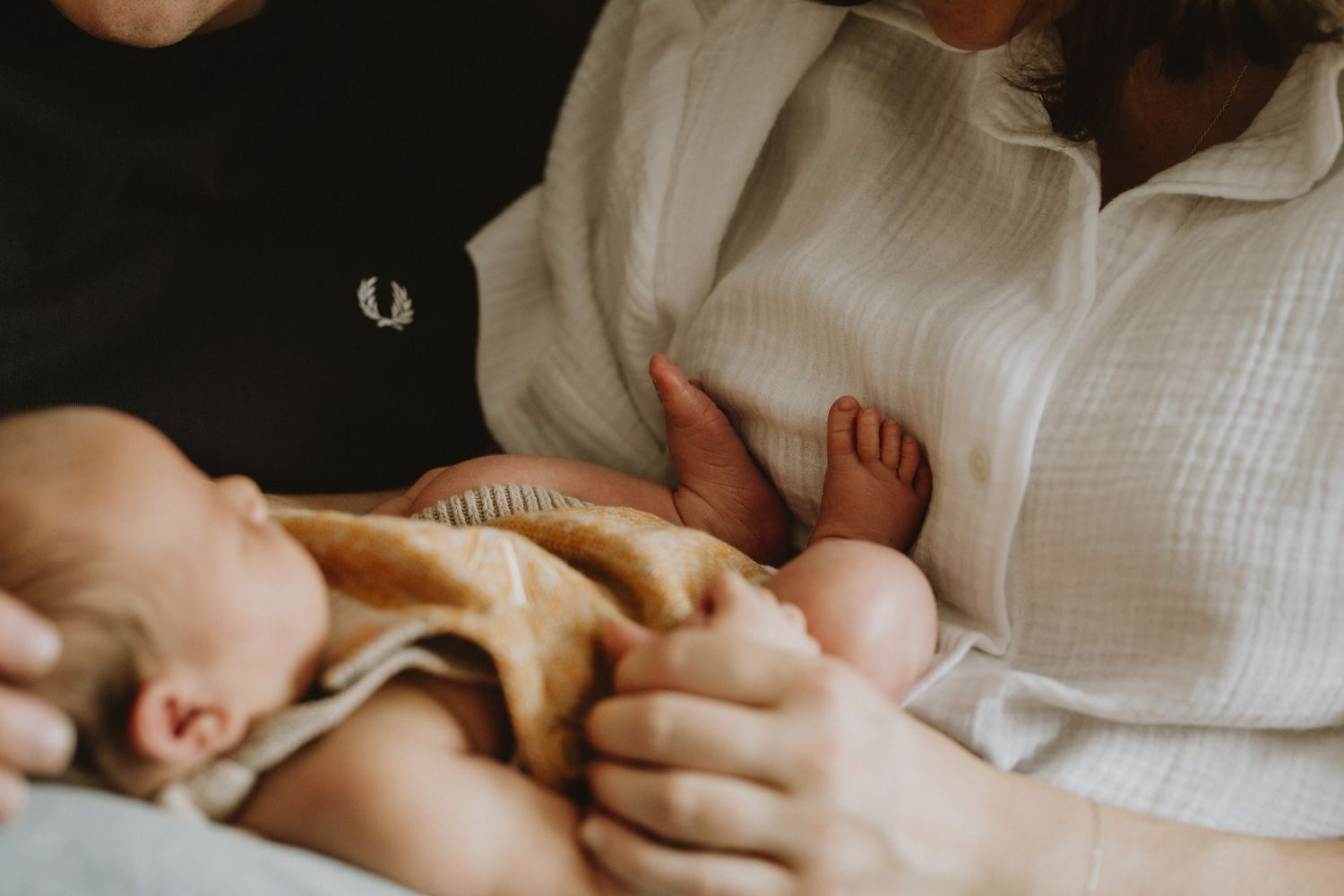 A small baby wrapped in a tan blanket rests peacefully while being held in someone's arms.