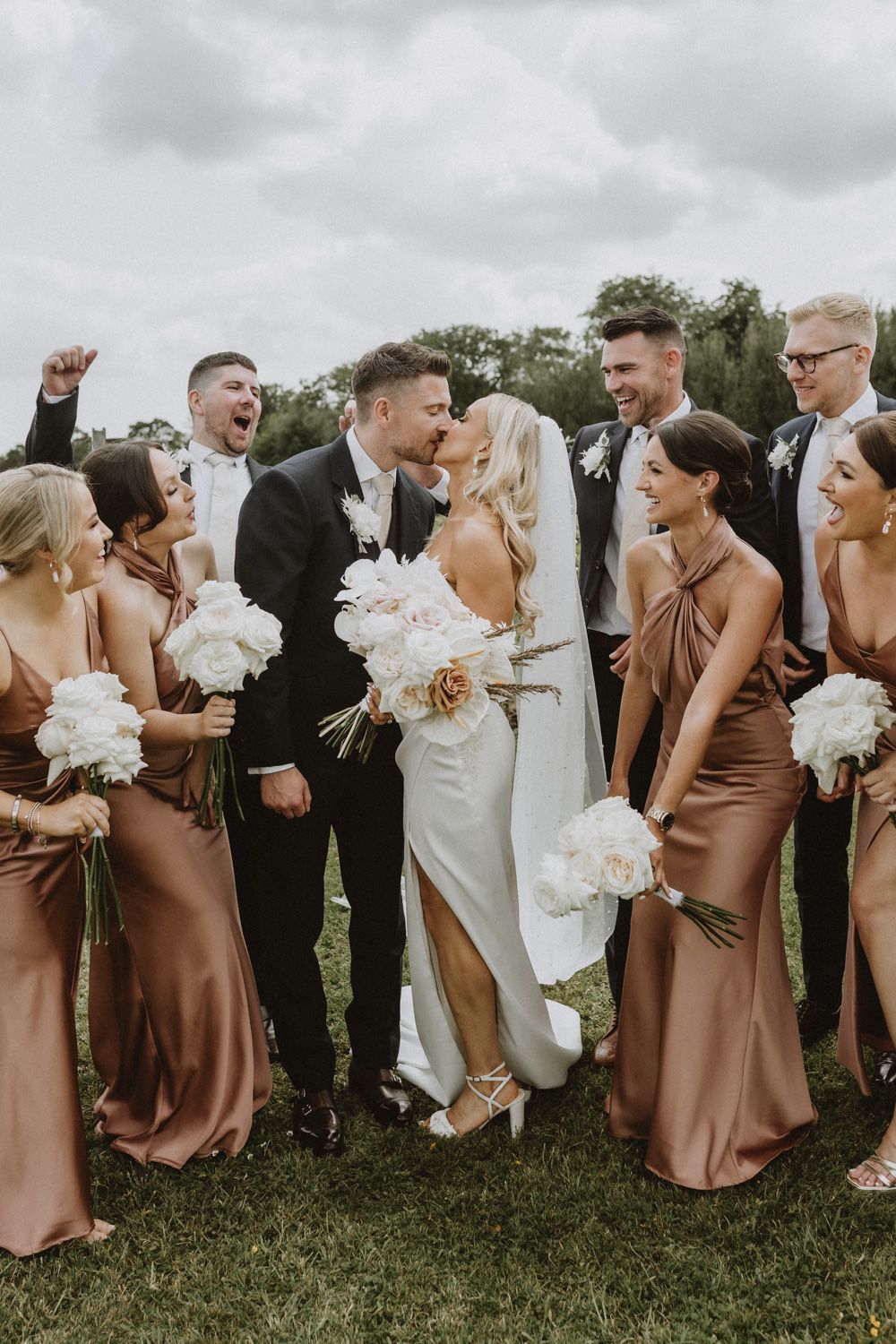 Wedding party laughs together while standing in a line outdoors.