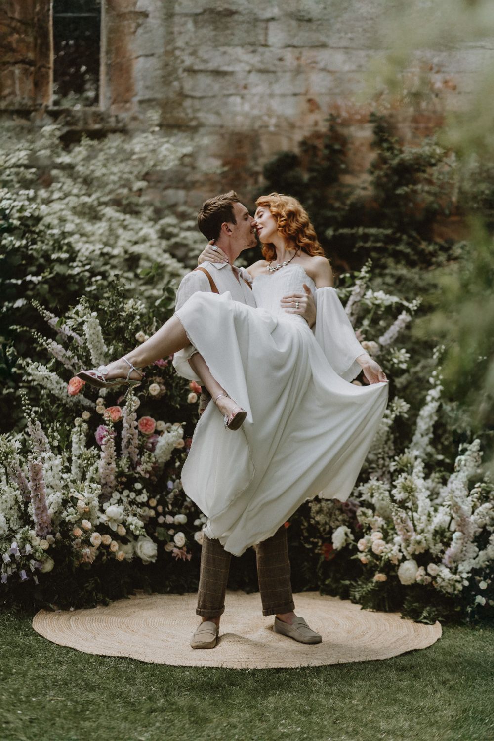 Joyful wedding moment in front of stone wall surrounded by blooming flowers.