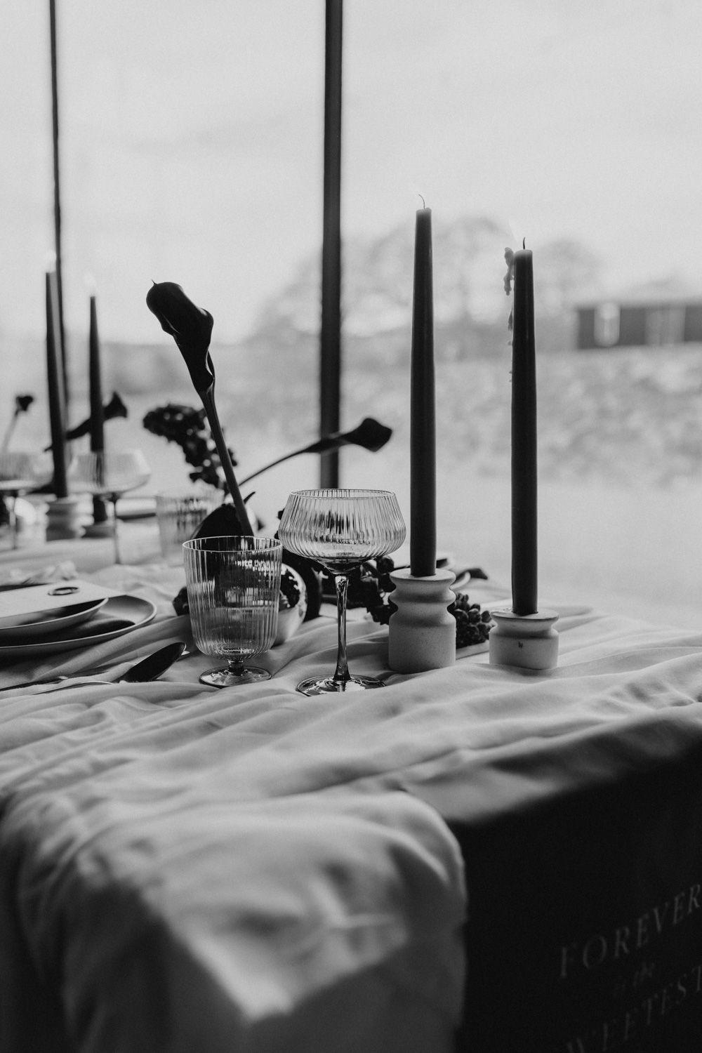 Black and white photo of table decor with tall black candles and vintage glassware.