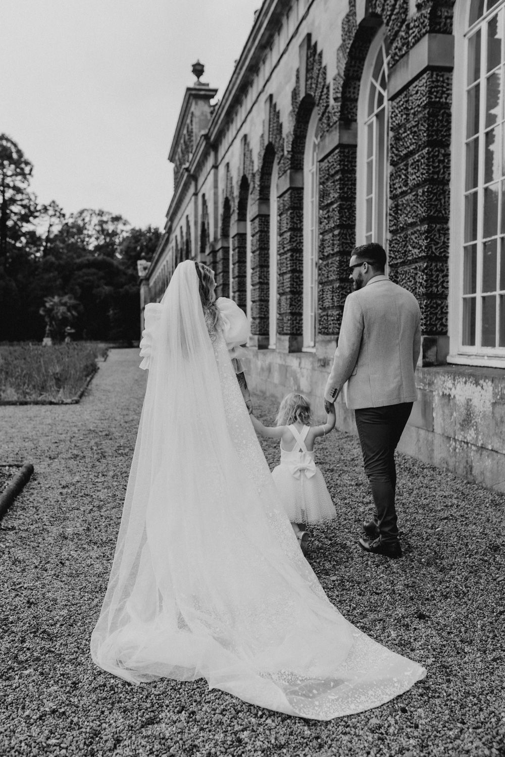 Wedding couple walking with child along historic building exterior.