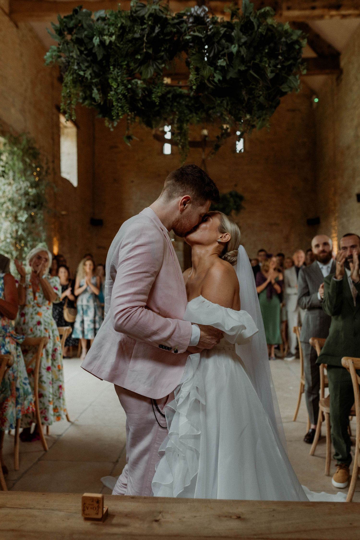 Couple shares their first dance in a rustic barn venue decorated with hanging greenery.