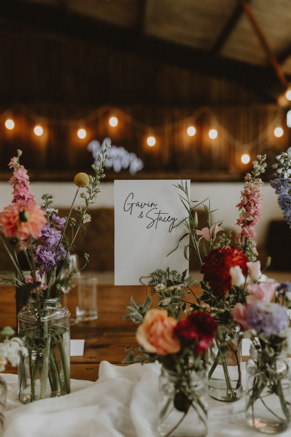 Rustic wedding table decorations with colorful wildflowers in glass jars and name cards.