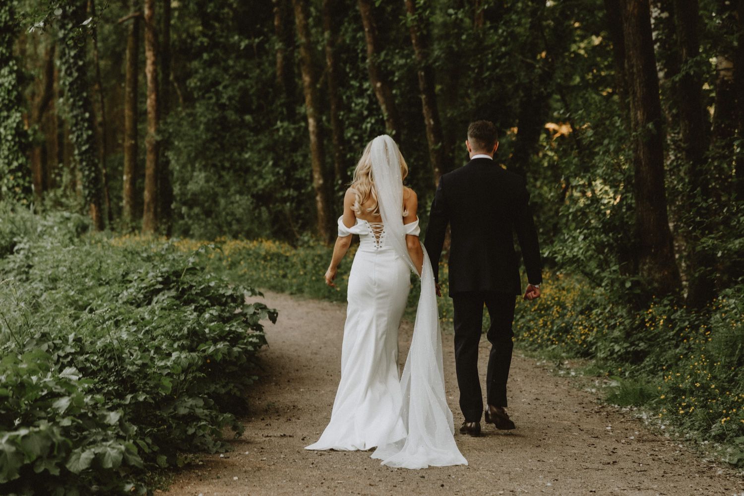 Wedding couple walks together through wooded path.