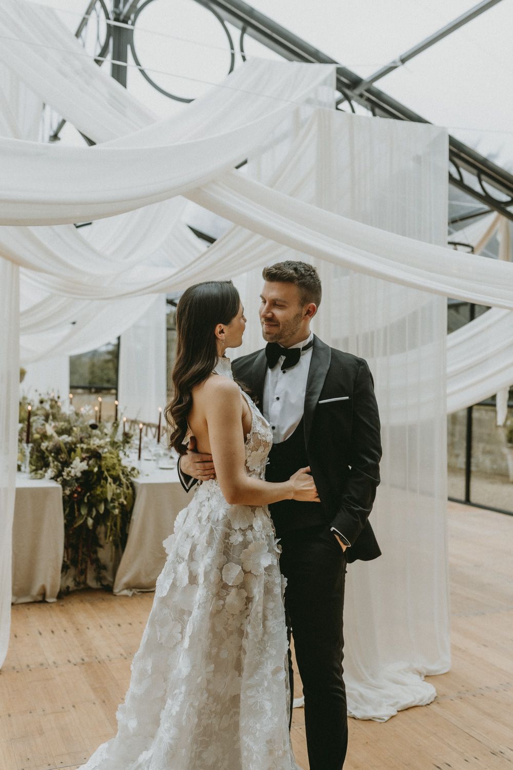 Intimate wedding celebration in an elegant white-draped venue with romantic lighting.