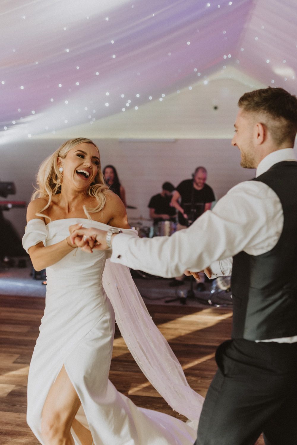 Wedding couple dances energetically under tent lighting.