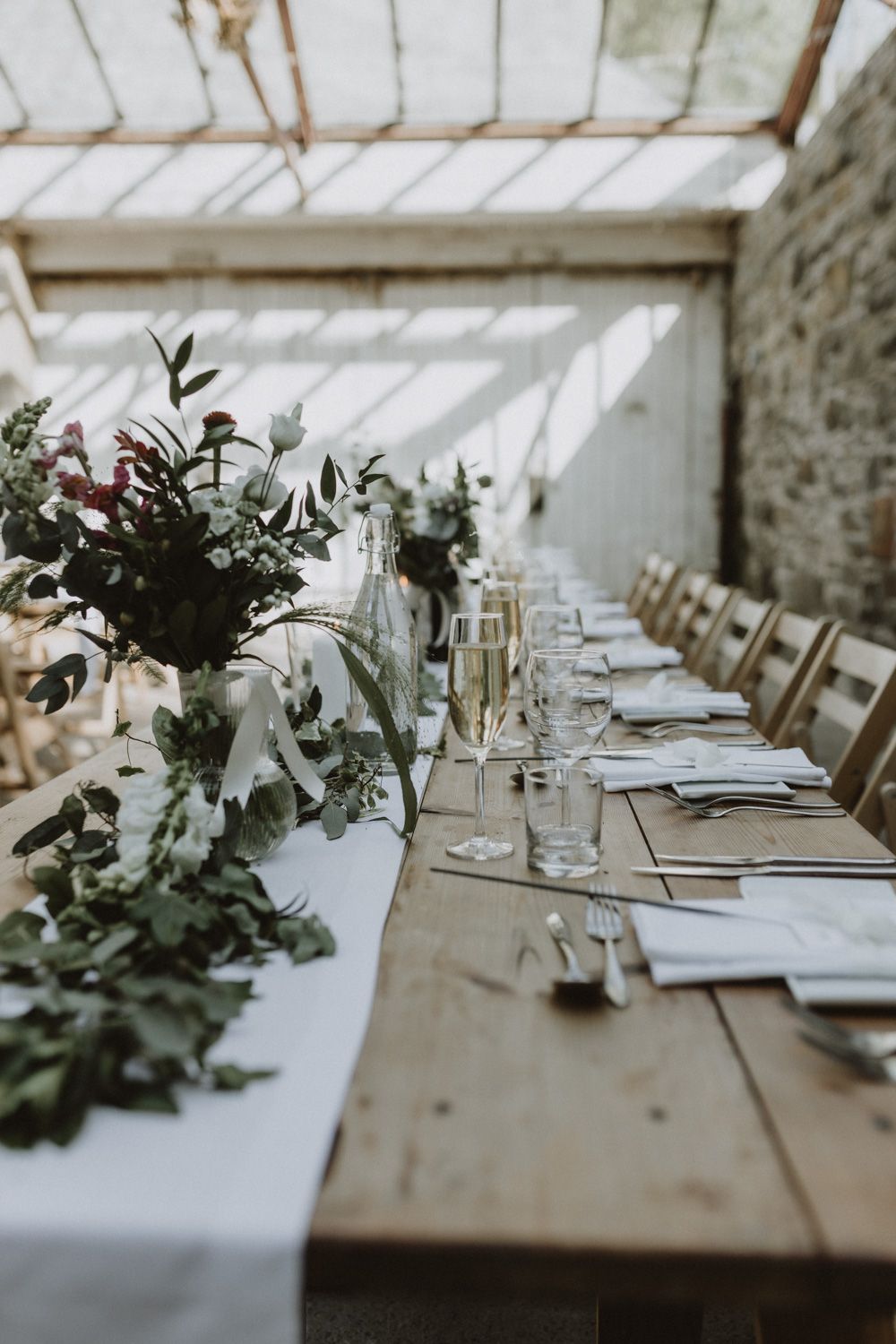 Elegant wedding reception tables with white linens and greenery decorations in a bright venue.