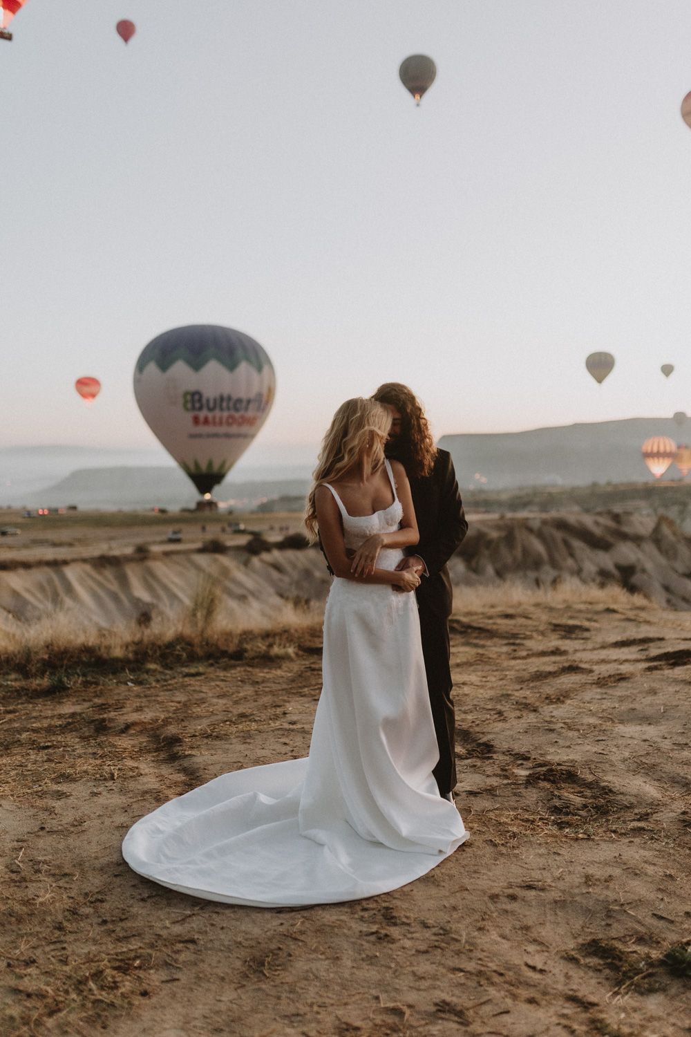 Hot air balloons float in the background of a desert landscape wedding scene.