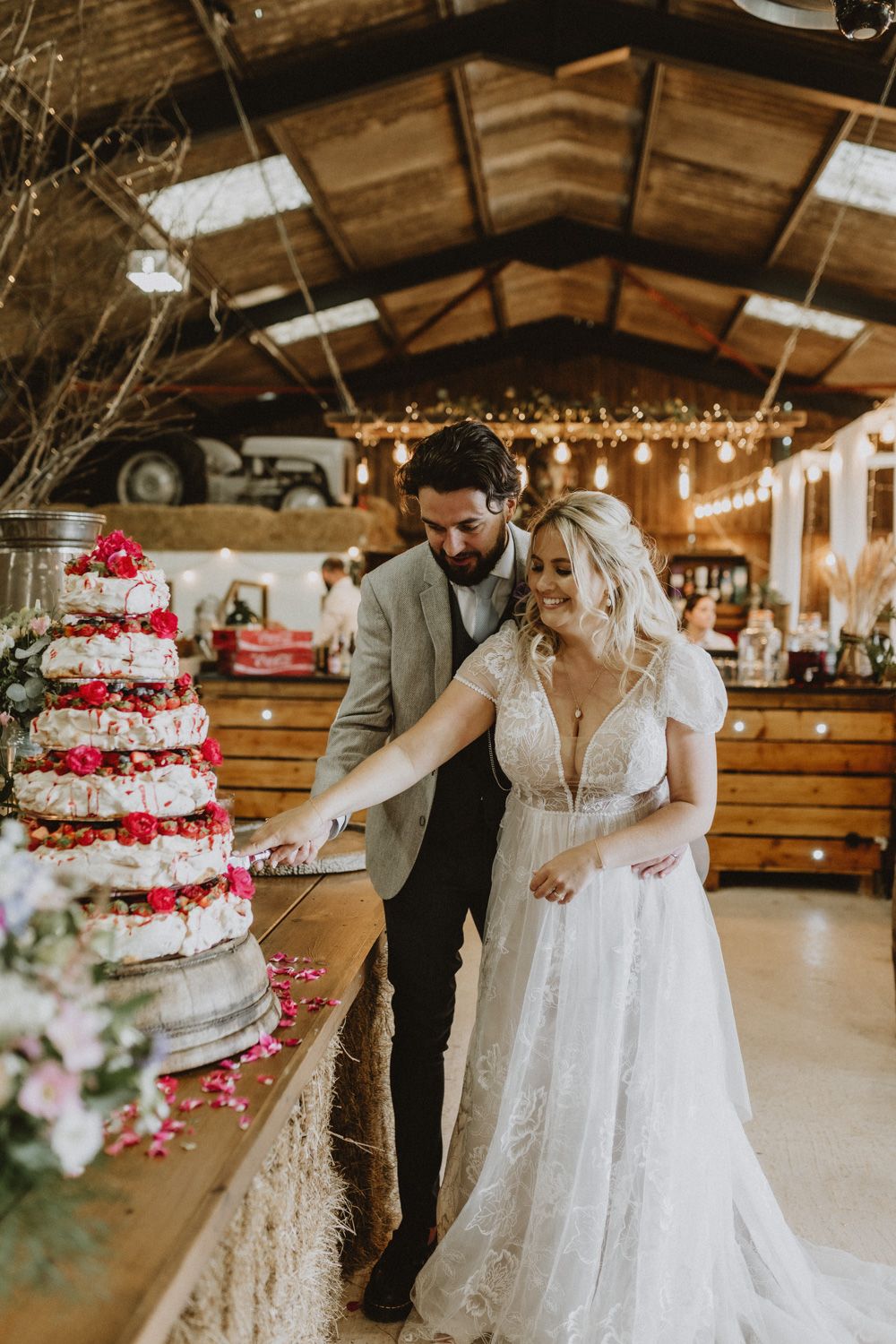A couple cuts their elegant white and red wedding cake in a rustic barn venue.